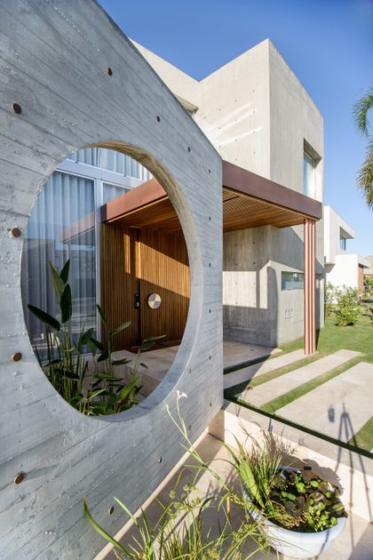 Fachada moderna brutalista con arco de hormigón y puerta de madera — proyecto Casa Pez, por Barrionuevo Arquitects, en B1648 Tigre