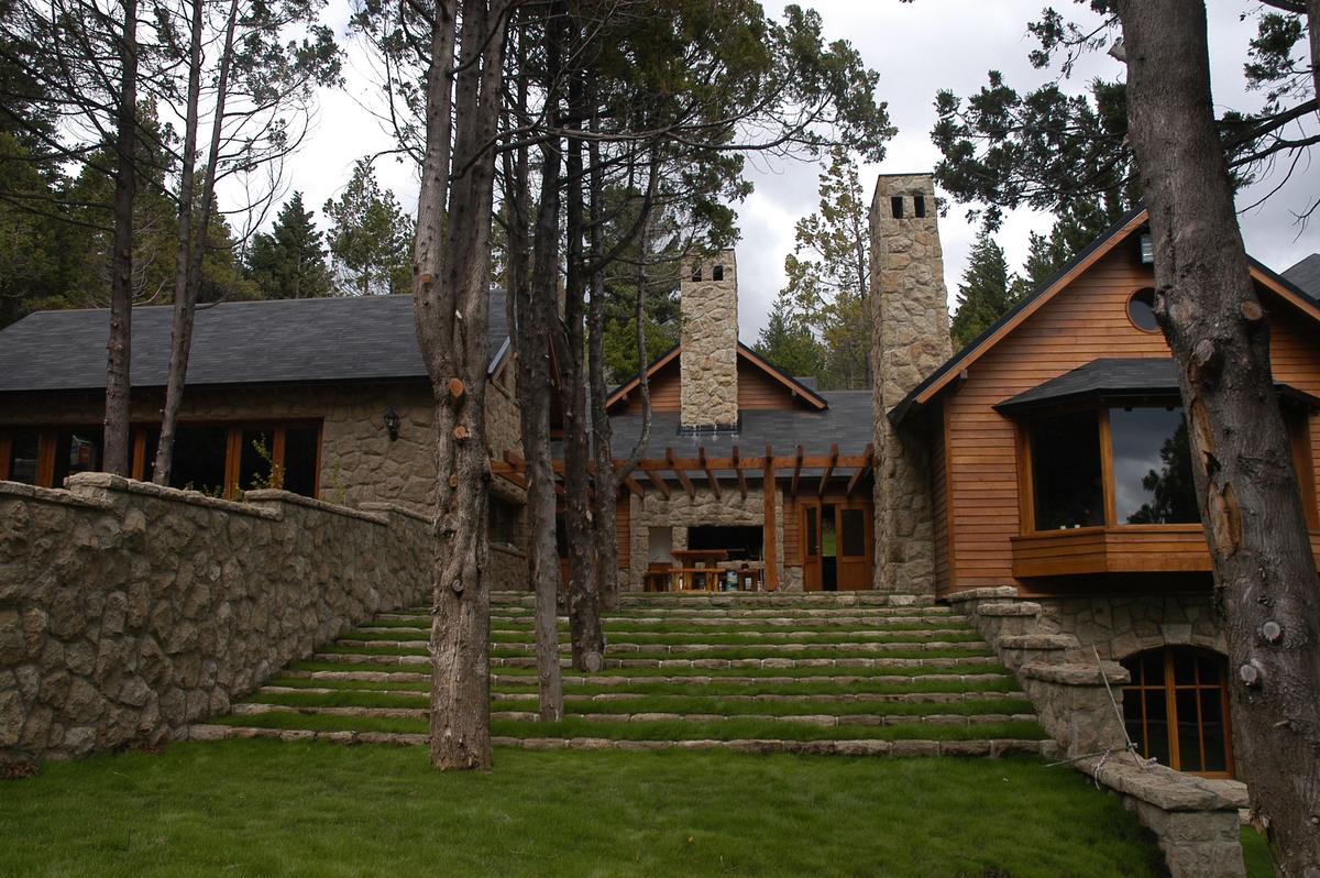 Fachada rústica de pedra com escadas em terraço e montanha — projeto Corrientes del Nahuel, por Ricardo Pereyra Iraola, em Bariloche