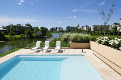 Piscina moderna con reposeras blancas junto a un lago en un día soleado — proyecto Al agua, por Ricardo Pereyra Iraola , en Nordelta
