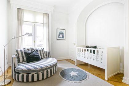 Dormitorio de bebé moderno con cuna y banco rayado, piso de madera — proyecto Libertador y Salguero, por Estudio Magrane, en CABA