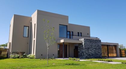 Fachada moderna con paredes de hormigón y piedra, y grandes ventanales — proyecto HARAS SANTA MARIA, por Ramirez Arquitectura, en Escobar