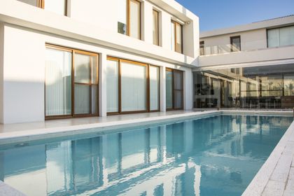 Amplia piscina moderna junto a fachada blanca y cristal — proyecto CASA GOLF, por Ramirez Arquitectura, en Nordelta