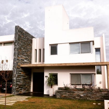 Fachada moderna blanca con detalles de piedra y amplios ventanales — proyecto Jardín Claret C, por Blussand Tosco, en Córdoba