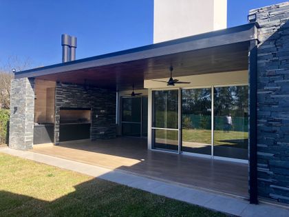 Parrilla exterior moderna con techo de madera oscura y paredes de piedra — proyecto Manantiales Z, por Blussand Tosco, en Córdoba
