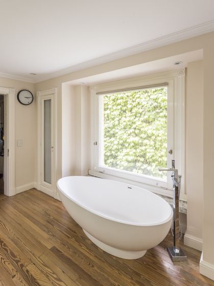 Bano moderno con banera ovalada blanca y gran ventanal hacia jardin — proyecto The Classic, por BAS Y GARCIA , en San Isidro