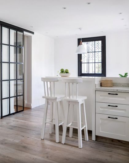 Cocina minimalista blanca con isla, sillas altas y ventanal con marco negro — proyecto Olivos, por Biaus Pieres Arquitectura