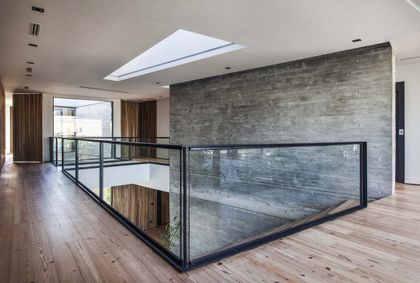 Pasillo de doble altura con escalera y barandal de vidrio ahumado — proyecto Casa India , por Estudio Simbiosis