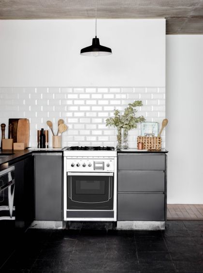 Cocina minimalista con mesada negra, azulejos blancos y estufa central — proyecto Casa Punta Chica , por Estudio Simbiosis, en Punta Chica