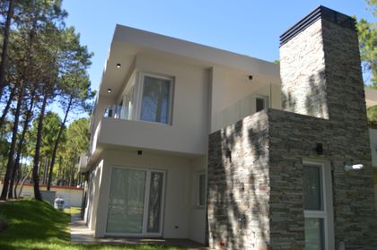 Fachada moderna con chimenea de piedra en bosque — proyecto PINAMAR NORTE, por LADAGA-RUARTE-Pinamar, en Pinamar