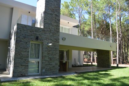 Fachada moderna con torre de piedra y balcón voladizo — proyecto PINAMAR NORTE, por LADAGA-RUARTE-Pinamar, en Pinamar
