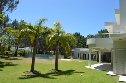 Jardín moderno con palmeras y piscina cerca de casa blanca — proyecto LA HERRADURA - Boulevard I, por LADAGA-RUARTE-Pinamar, en Pinamar