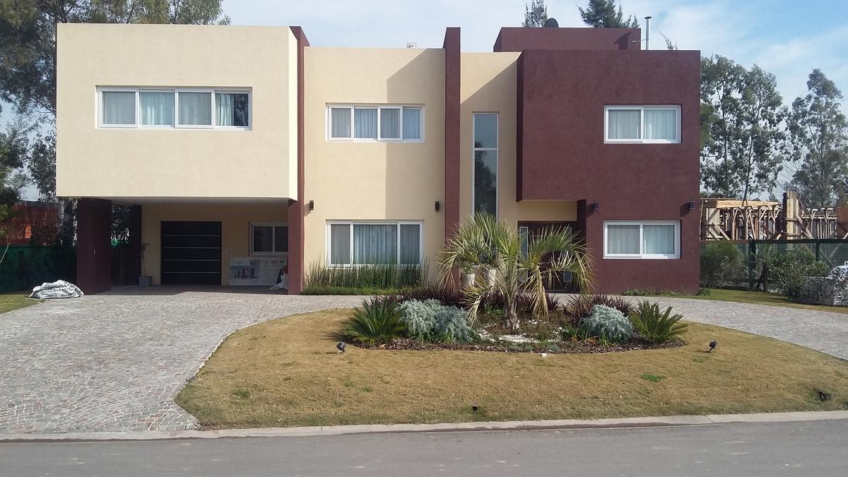 Casa moderna geométrica con fachada de hormigón en tonos beige y burdeos — proyecto Terralagos 1, por Arquitecto Oscar Sanguineti, en Canning