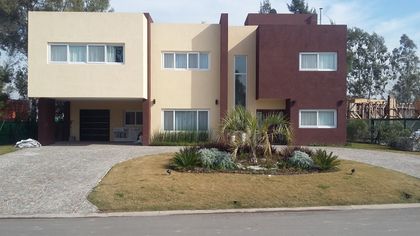 Casa moderna geométrica con fachada de hormigón en tonos beige y burdeos — proyecto Terralagos 1, por Arquitecto Oscar Sanguineti, en Canning