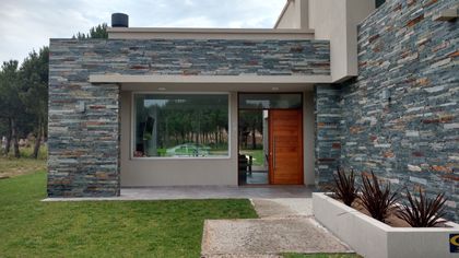 Fachada moderna con piedra en capas y grandes ventanales — proyecto LA HERRADURA - Cul de Sac De La Cincha, por LADAGA-RUARTE-Pinamar, en Pinamar