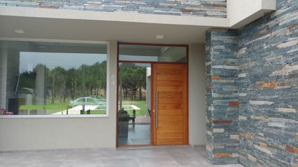 fachada moderna con puerta de madera y piedra — proyecto LA HERRADURA - Cul de Sac De La Cincha, por LADAGA-RUARTE-Pinamar, en Pinamar