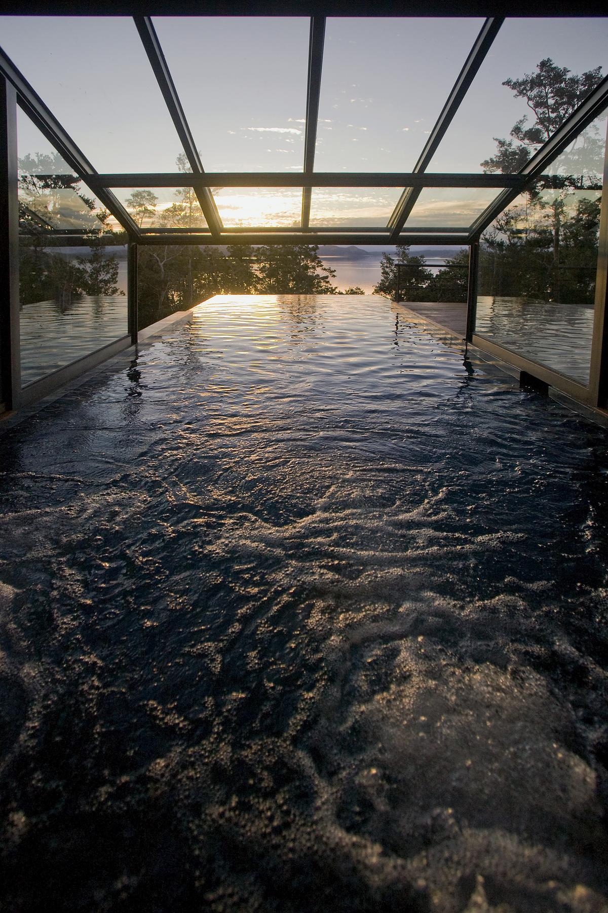 Área de piscina interna com vista para o pôr do sol e teto de vidro — projeto Casa Muelle de Piedra, por Sidoni & Asociados, em Villa La Angostura