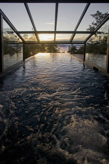 Piscina infinita interior con vista al atardecer y techo de cristal — proyecto Casa Muelle de Piedra, por Sidoni & Asociados, en Villa La Angostura