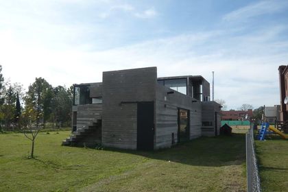 Casa moderna con fachada gris oscuro y grandes ventanales en jardín verde — proyecto Casa Canning, por Luciano Kruk, en Canning
