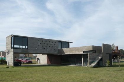 Casa contemporánea con fachada de hormigón y ladrillo, amplio jardín verde — proyecto Casa Canning, por Luciano Kruk, en Canning