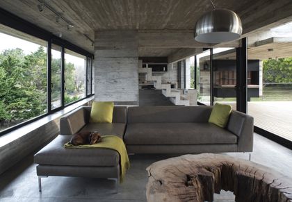 Living minimalista con sofa gris, ventanales amplios y hormigon visto — proyecto Casa Cariló, por Luciano Kruk, en Cariló
