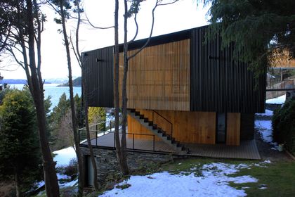 Fachada moderna con detalles en madera frente a un lago nevado — proyecto Casa Península San Pedro, por Servente Larrazabal Arq, en Bariloche