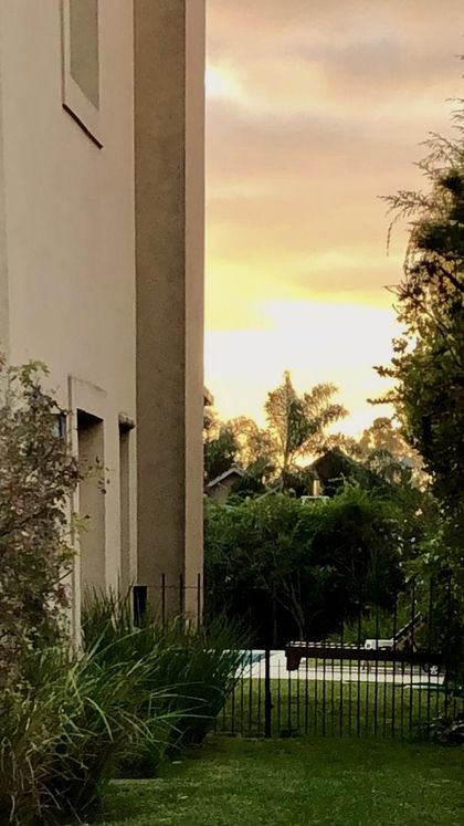 Jardín patio con fachada moderna y atardecer dorado en el fondo — proyecto Los Galapagos Garín, por Marconi Silva Arquitectos, en Garin