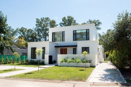 Fachada moderna blanca de dos pisos con grandes ventanales y jardín minimalista — proyecto Bosque Chico, por Estudio Arq. María Sioli, en Garin