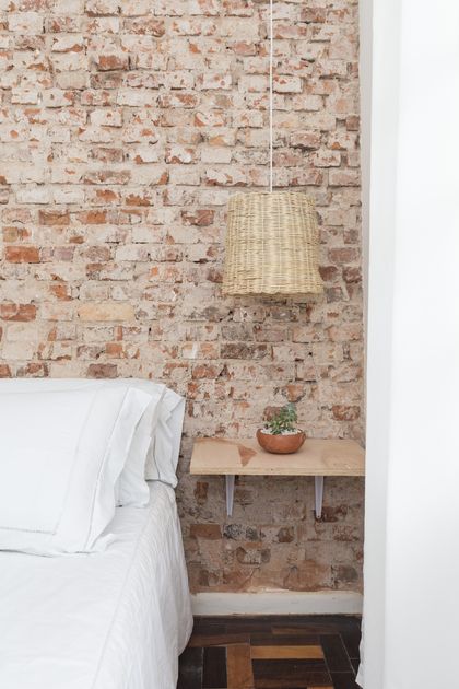 Dormitorio minimalista con pared de ladrillo visto y lámpara de mimbre — proyecto Roomie Coliving, por Camila Cavalheiro Arquiteta