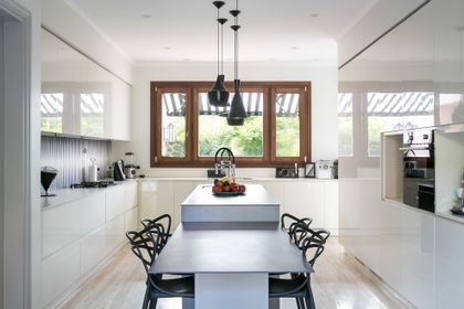 Cocina minimalista blanca con isla central y ventanal de madera — proyecto CasaLA, por Ricardo Pereyra Iraola 