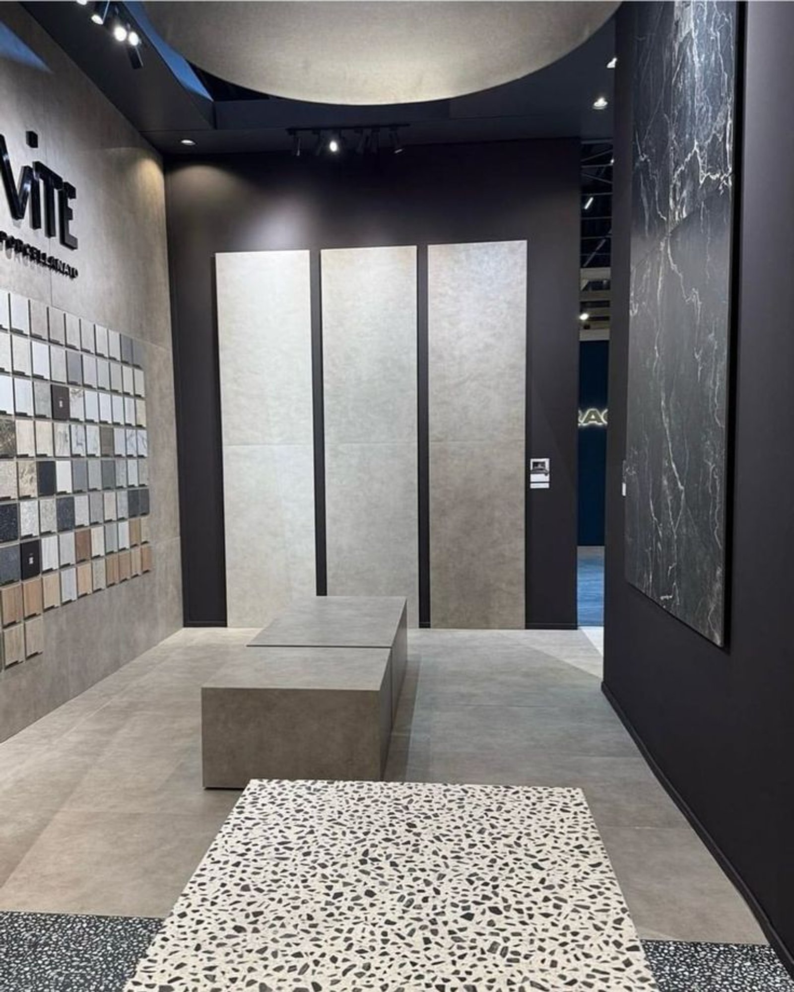 Sala de exposición de baldosas con muebles de cemento y pared de mármol — proyecto Expo Revestir 2025, por Vite Porcellanato, en São Paulo