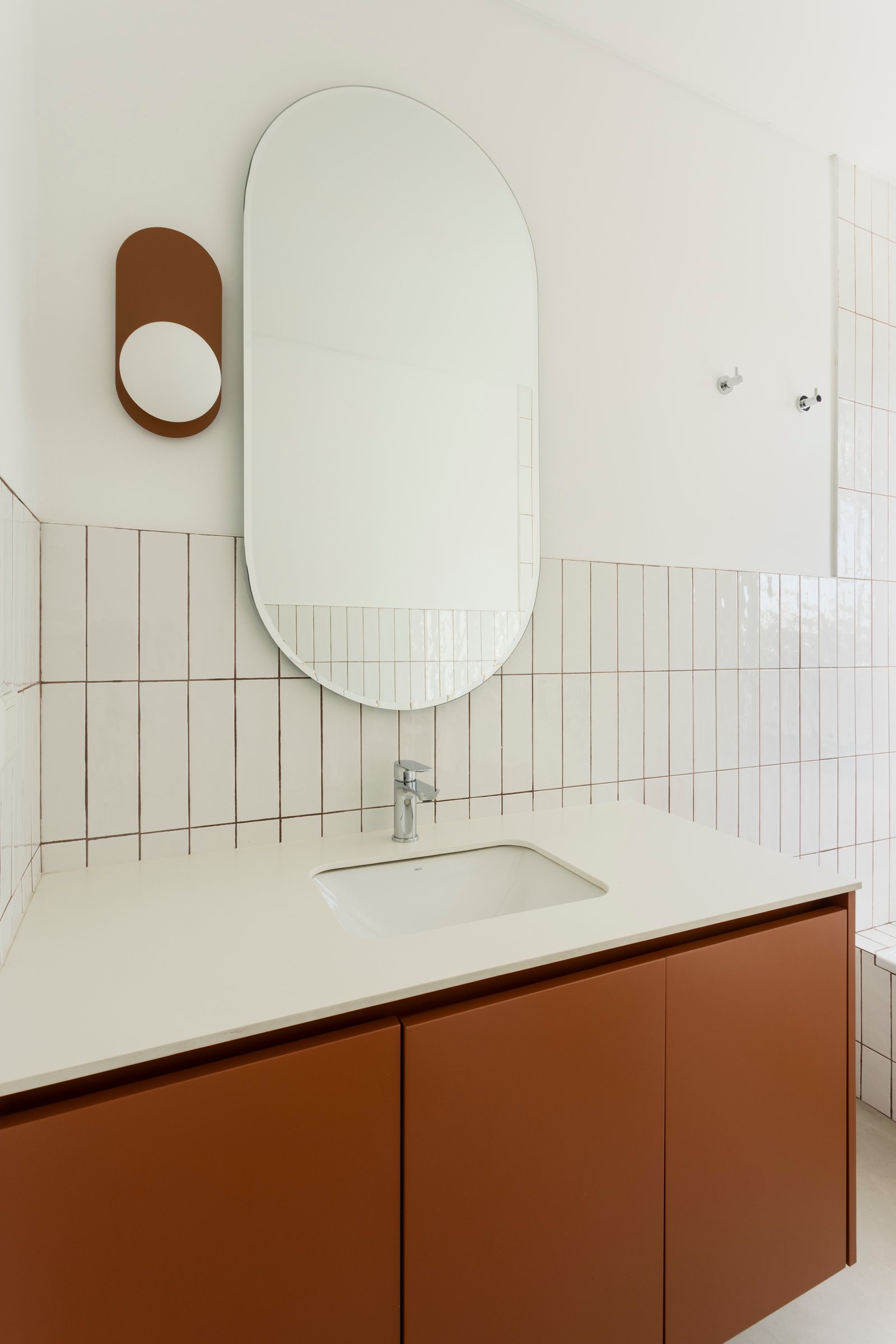 Baño moderno con espejo ovalado y mueble terracota — proyecto CASA CC, por Rastro Estudio, en San Isidro