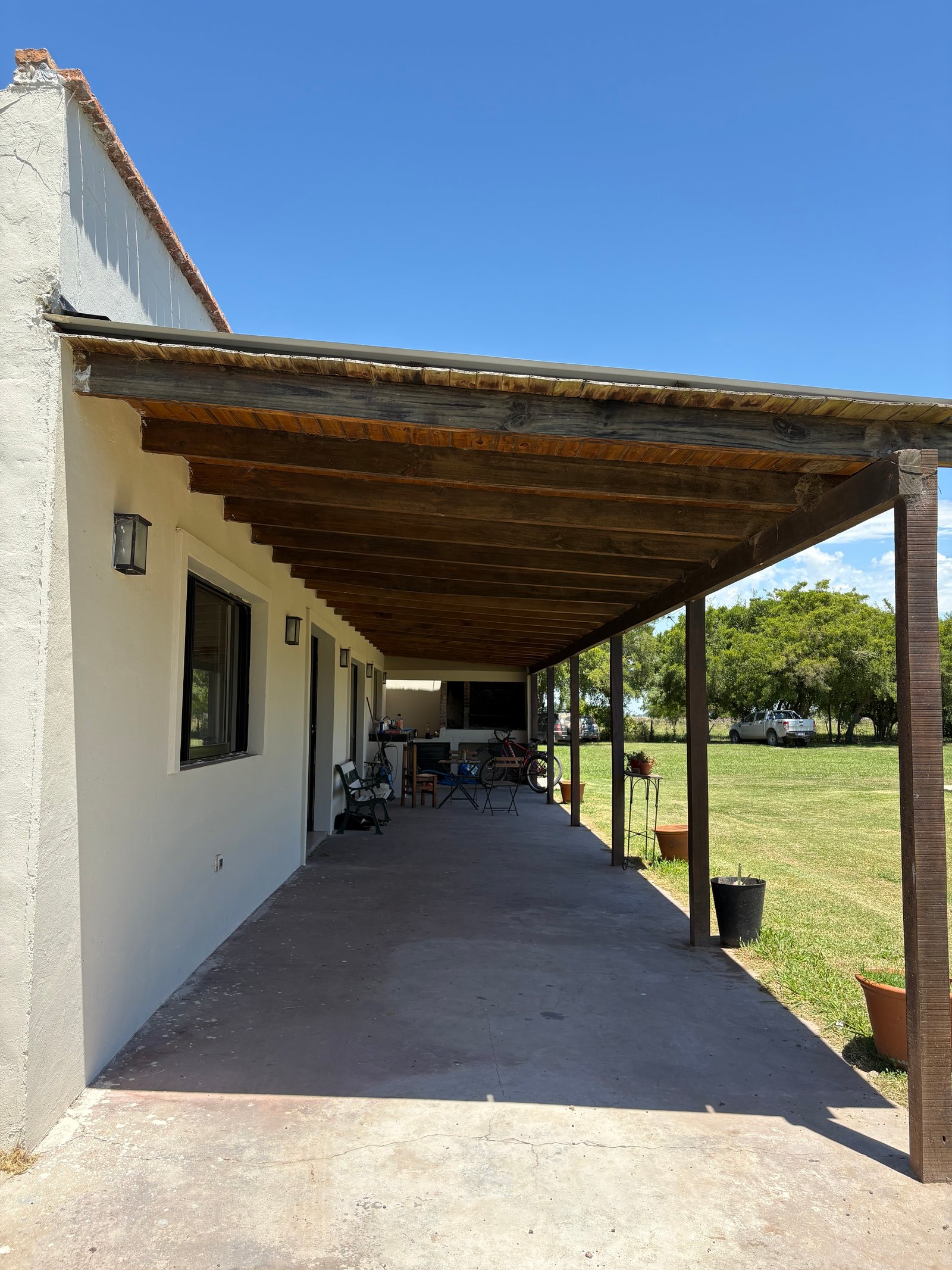 Fachada rústica con pérgola de madera y patio de cemento al aire libre — proyecto Reforma Casa de campo, Chascomus , por Estudio cardo, en Alsina 351
