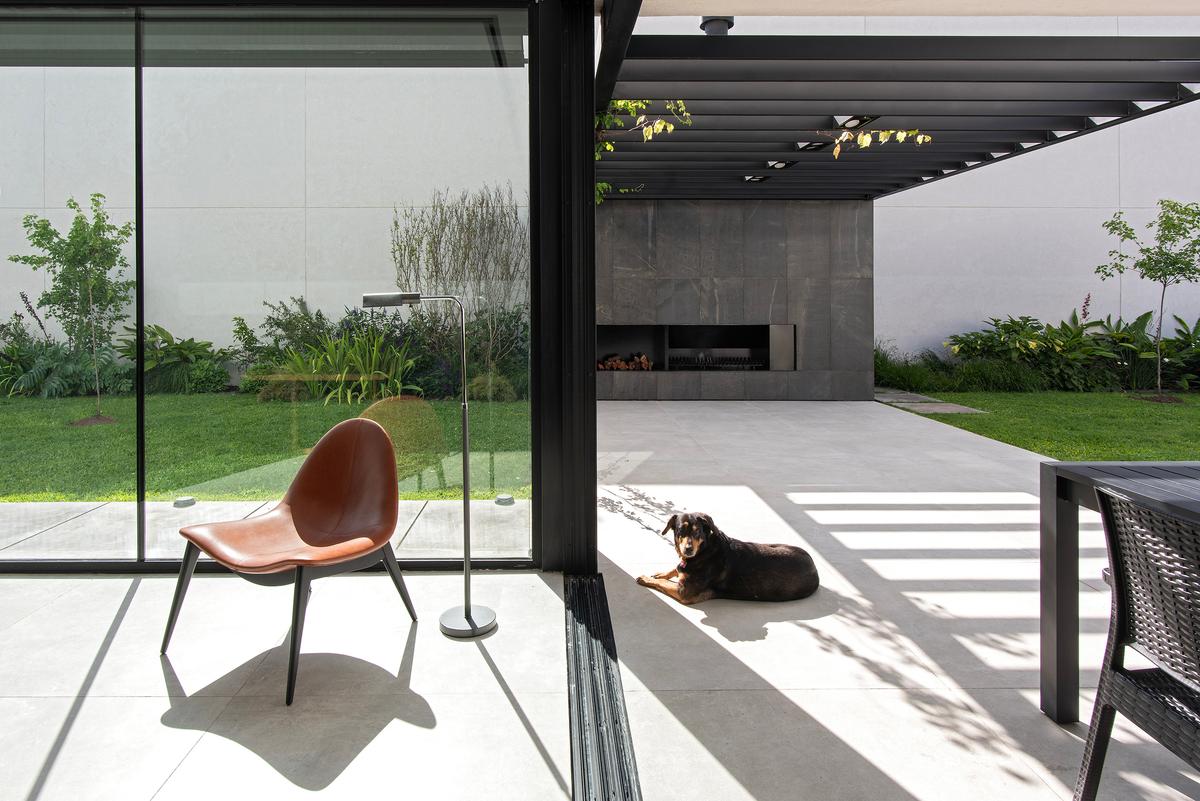 Área de estar externa moderna com poltronas pretas e cão — projeto CASA SD28, por GMARQ, em Buenos Aires
