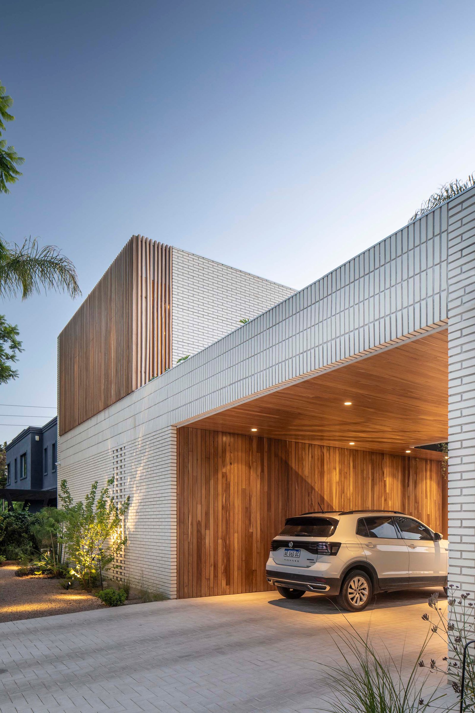Fachada moderna com tijolo branco e madeira, garagem integrada — projeto Casa Magnolia, por Estudio PK, em San Isidro