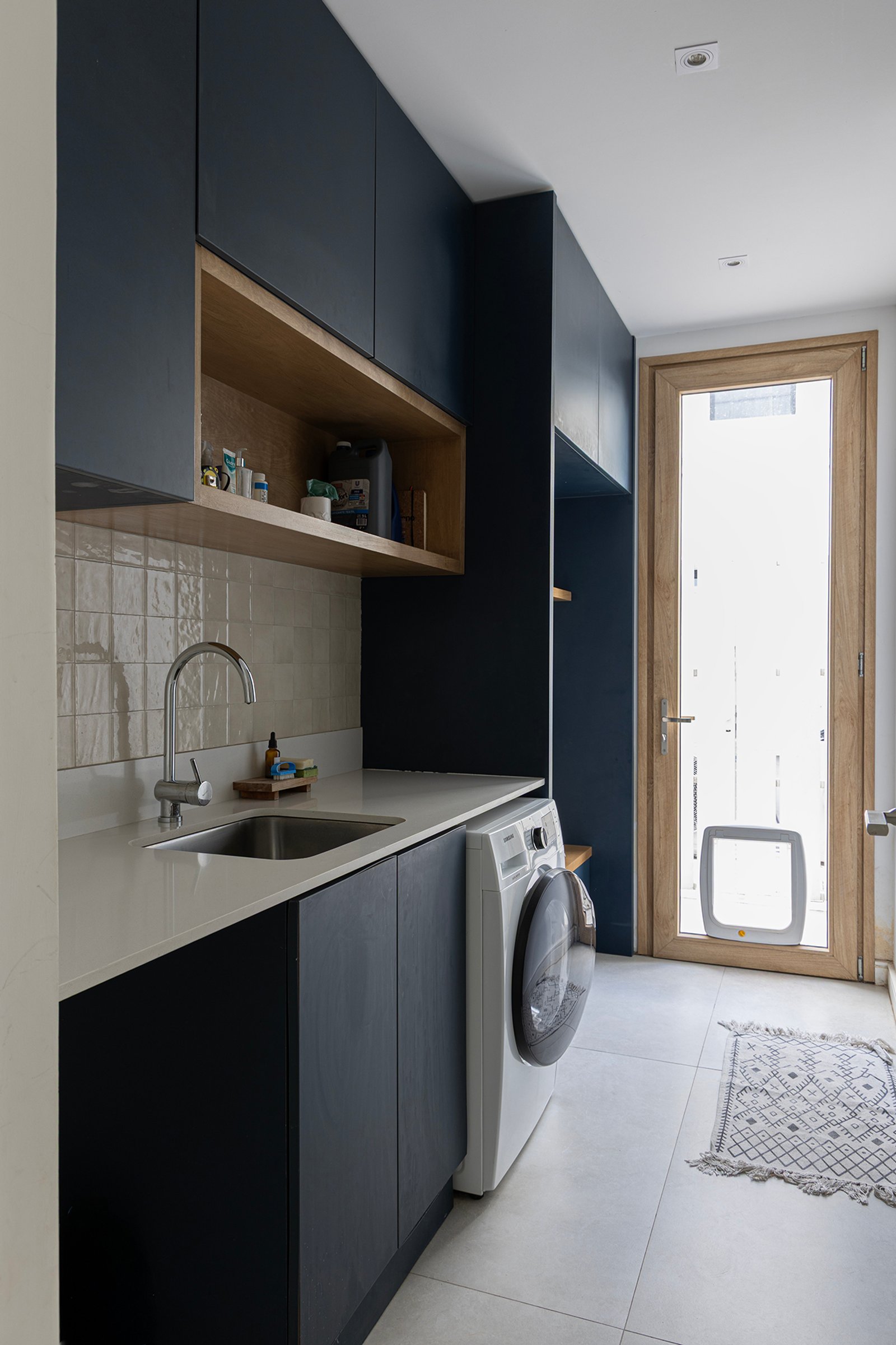 Lavadero moderno con muebles azules, mesada de piedra y puerta con trampilla para perro — proyecto Casa Al Agua - Grupo PAUTA, por Gaby Alfonso, en Belén de Escobar