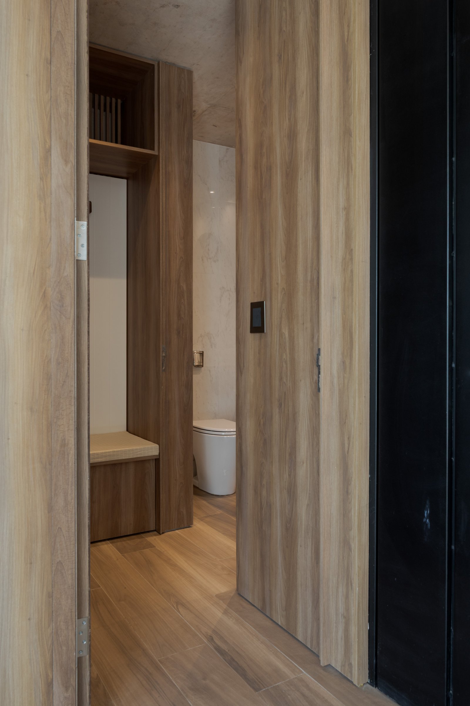 Corredor moderno com revestimento de madeira e lavabo integrado — projeto Casa PLANALTO, por Grupo CRBN, em Av. Pres. Perón 10298