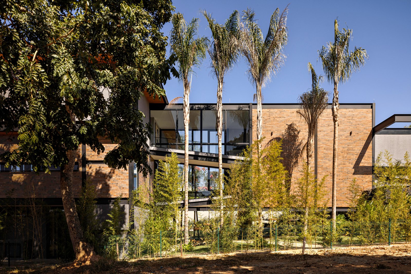 fachada moderna de tijolos com grandes janelas e árvores — projeto Casa do Lago, por dayala e rafael arquitetos associados, em Alexânia