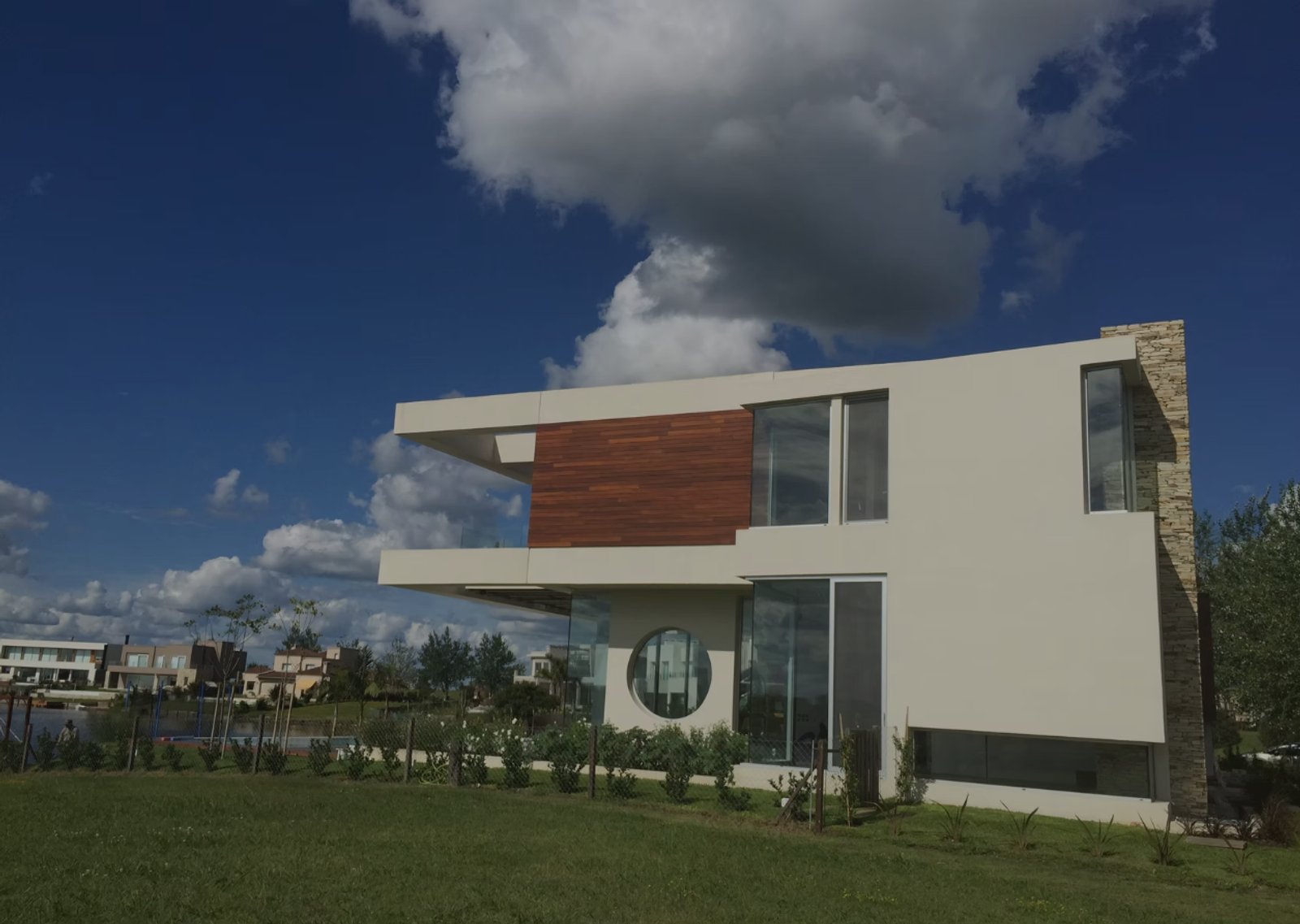 Fachada moderna con volúmenes geométricos, madera y piedra — proyecto Casa Cinta, por Barrionuevo Arquitects, en B2814 Los Cardales