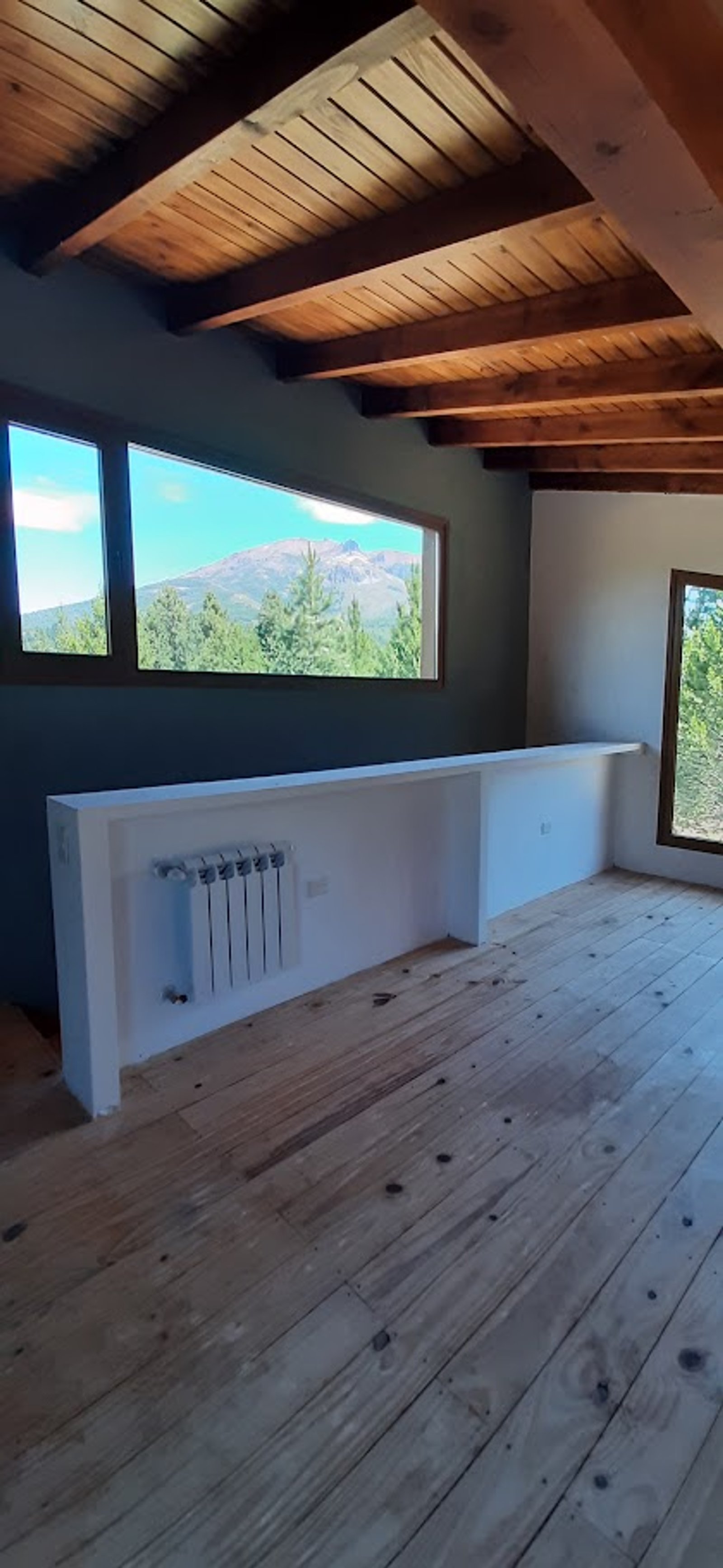 Habitación con piso de madera, vigas de madera y gran ventanal con vista a la montaña — proyecto Proyecto Casa SZ, por Arquitecta Grace Overgaard, en Acceso Al Challhuaco