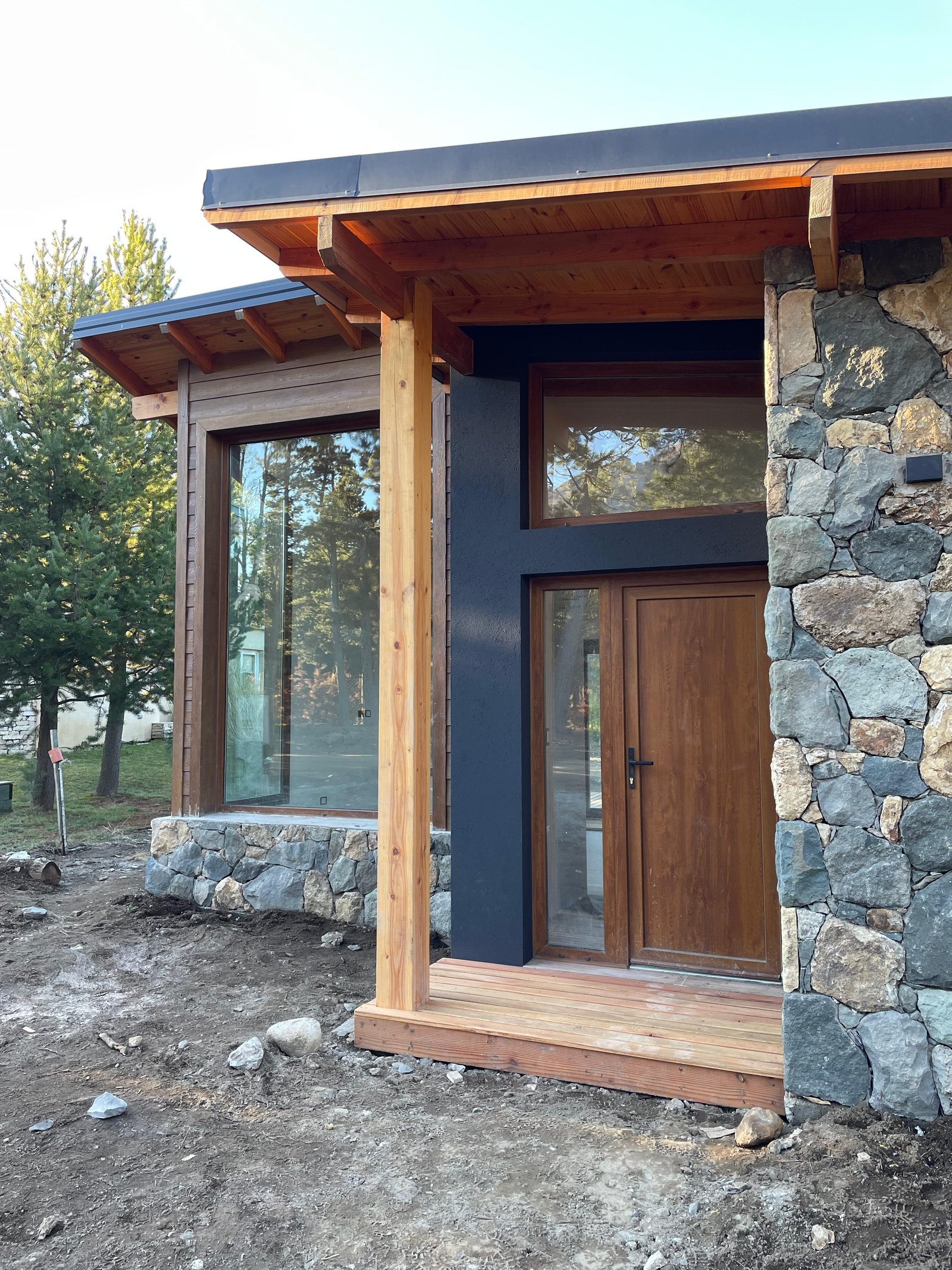 Fachada de casa moderna en construcción con detalles rústicos — proyecto Casa Arcoiris, por Arquitecta Grace Overgaard, en Acceso Al Challhuaco