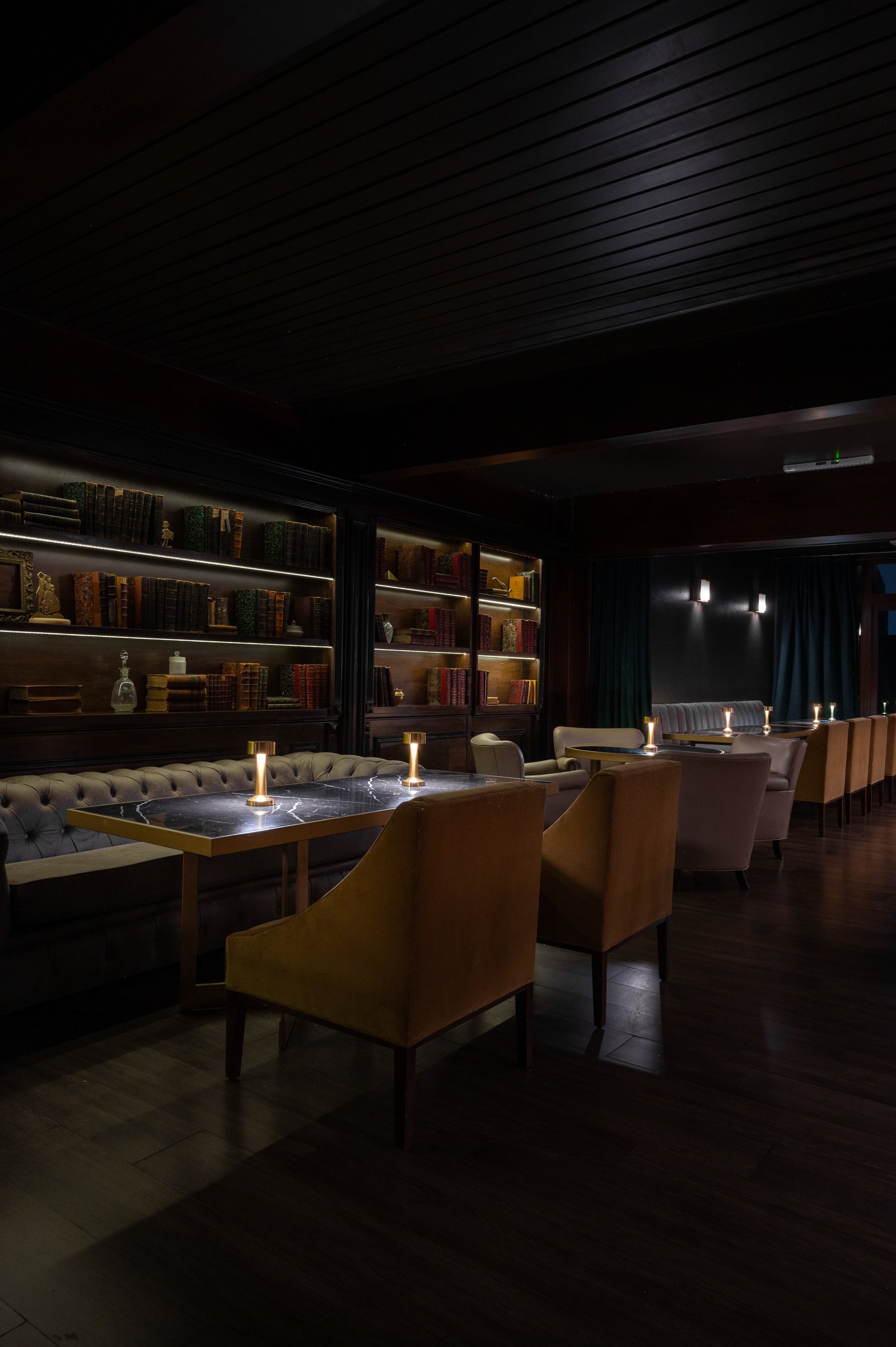 Sala com biblioteca, assentos de tecido e iluminação quente — projeto PRESIDENTE BAR HIPODROMO, por AB ARQUITECTURA, em San Isidro