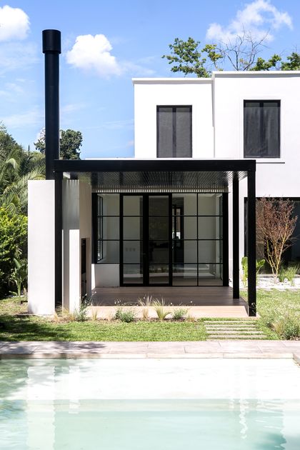 Fachada moderna blanca con chimenea negra y piscina en jardín — proyecto Bosque Chico, por Estudio Arq. María Sioli, en Garin