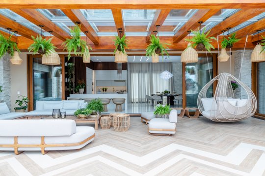 Amplia terraza moderna con pérgola de madera, sillón colgante y mobiliario blanco — proyecto Projeto Destaque Club&Casa, por OKA ARQUITETURA
