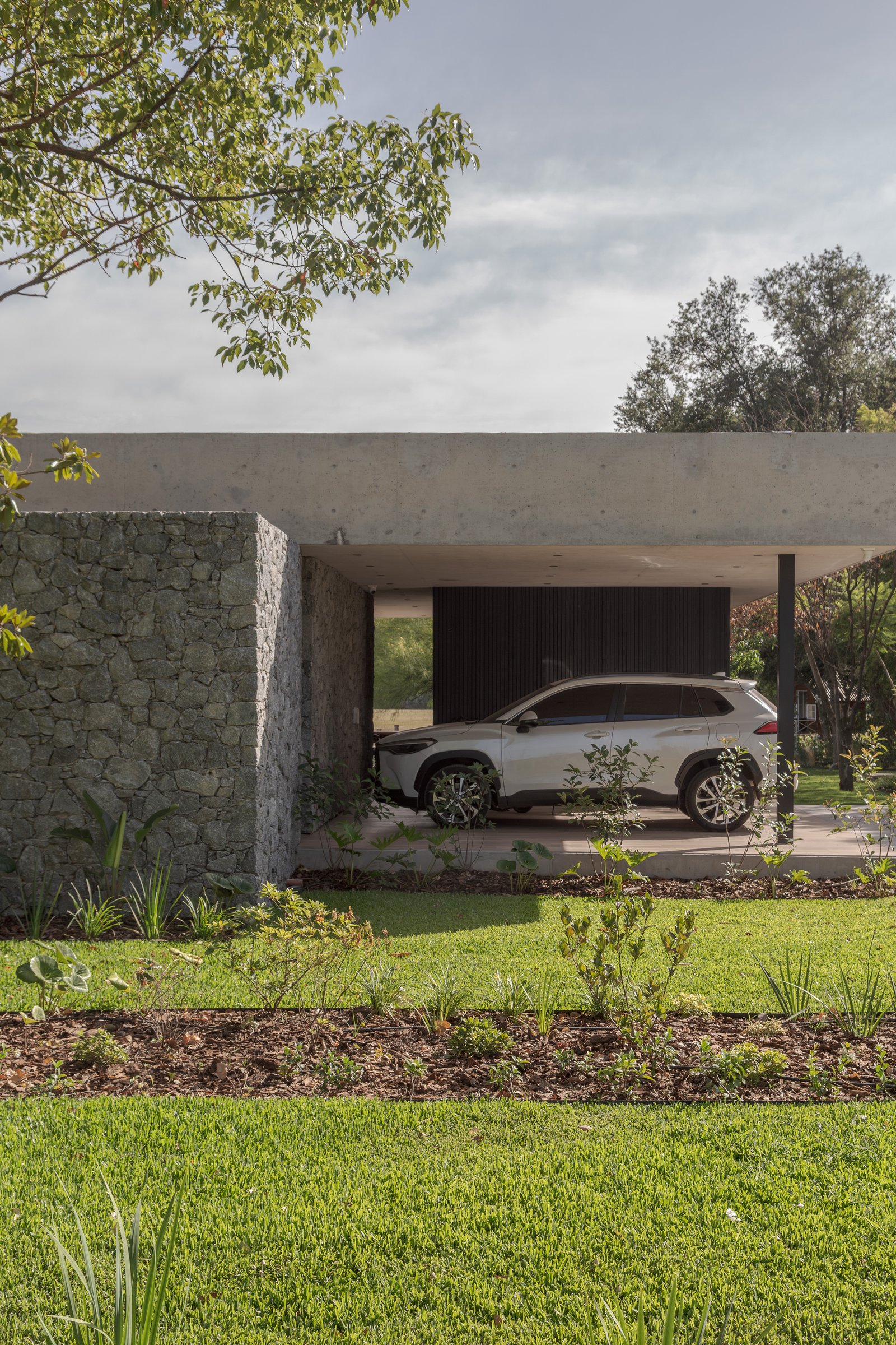 Fachada moderna con muro de piedra y cochera de concreto — proyecto Casa PLANALTO, por Grupo CRBN, en Av. Pres. Perón 10298