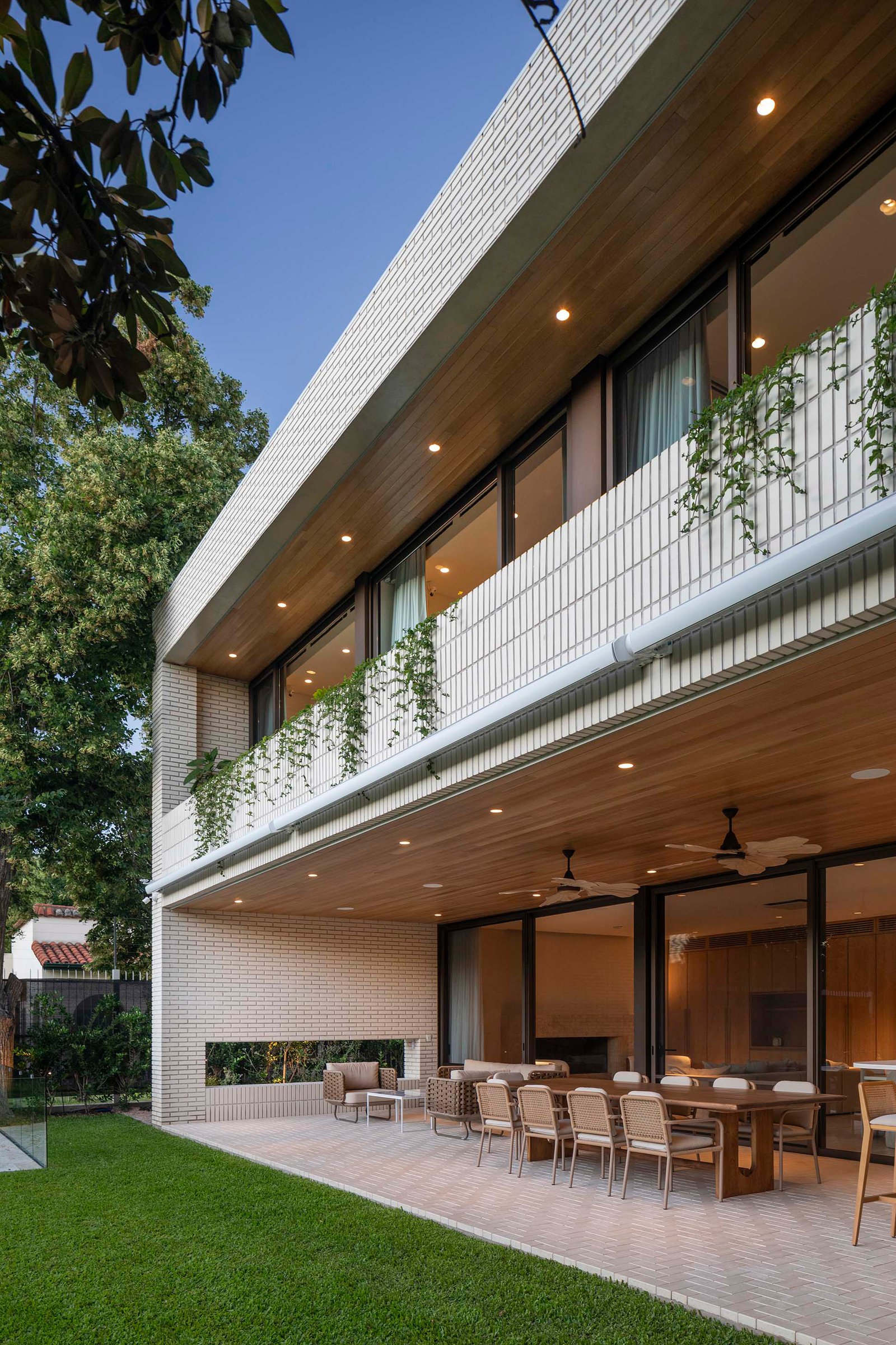 Patio moderno con techo de madera, muebles de rattan y mucha vegetación — proyecto Casa Magnolia, por Estudio PK, en San Isidro