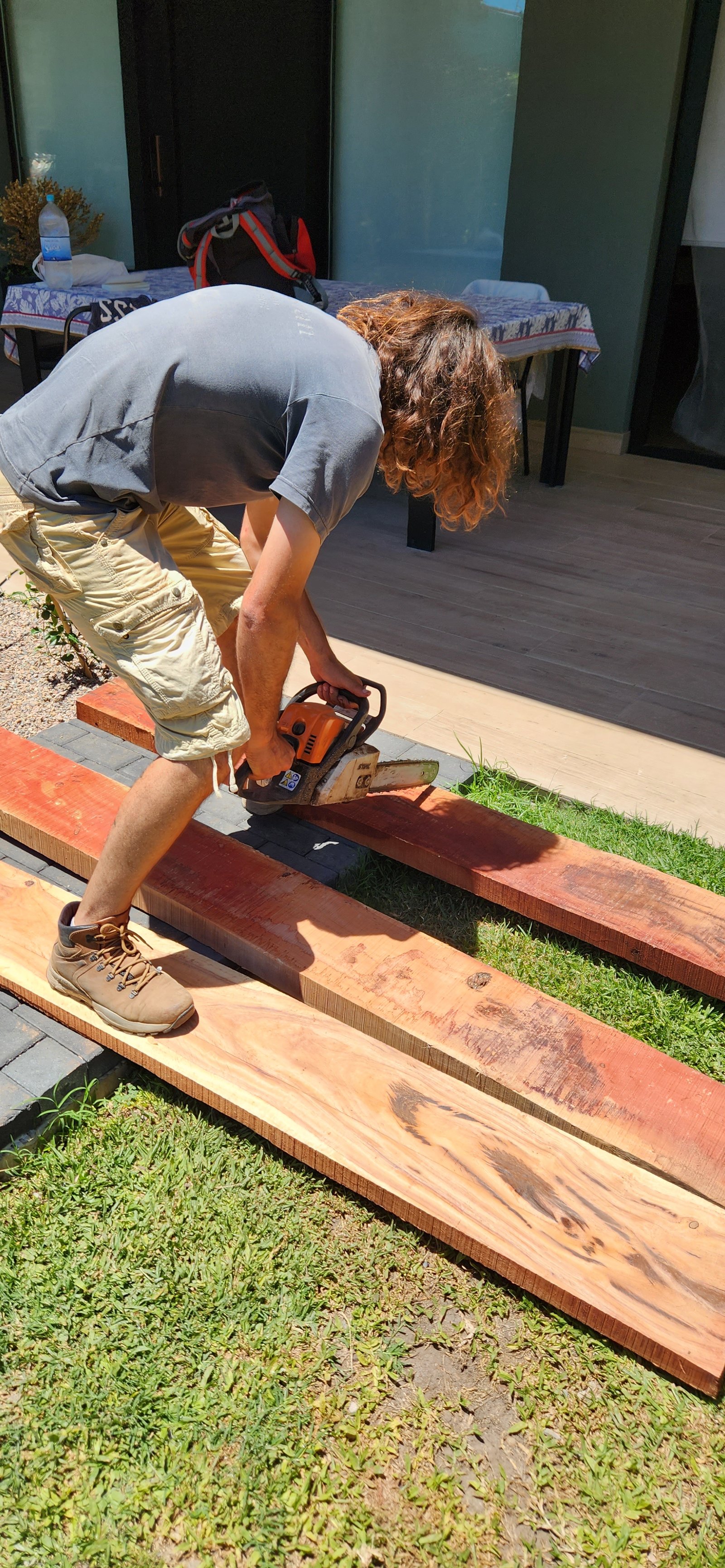 Hombre trabajando con motosierra en tablones de madera al aire libre — proyecto Casa SF, por Estudio Rifahi, en Bella Vista