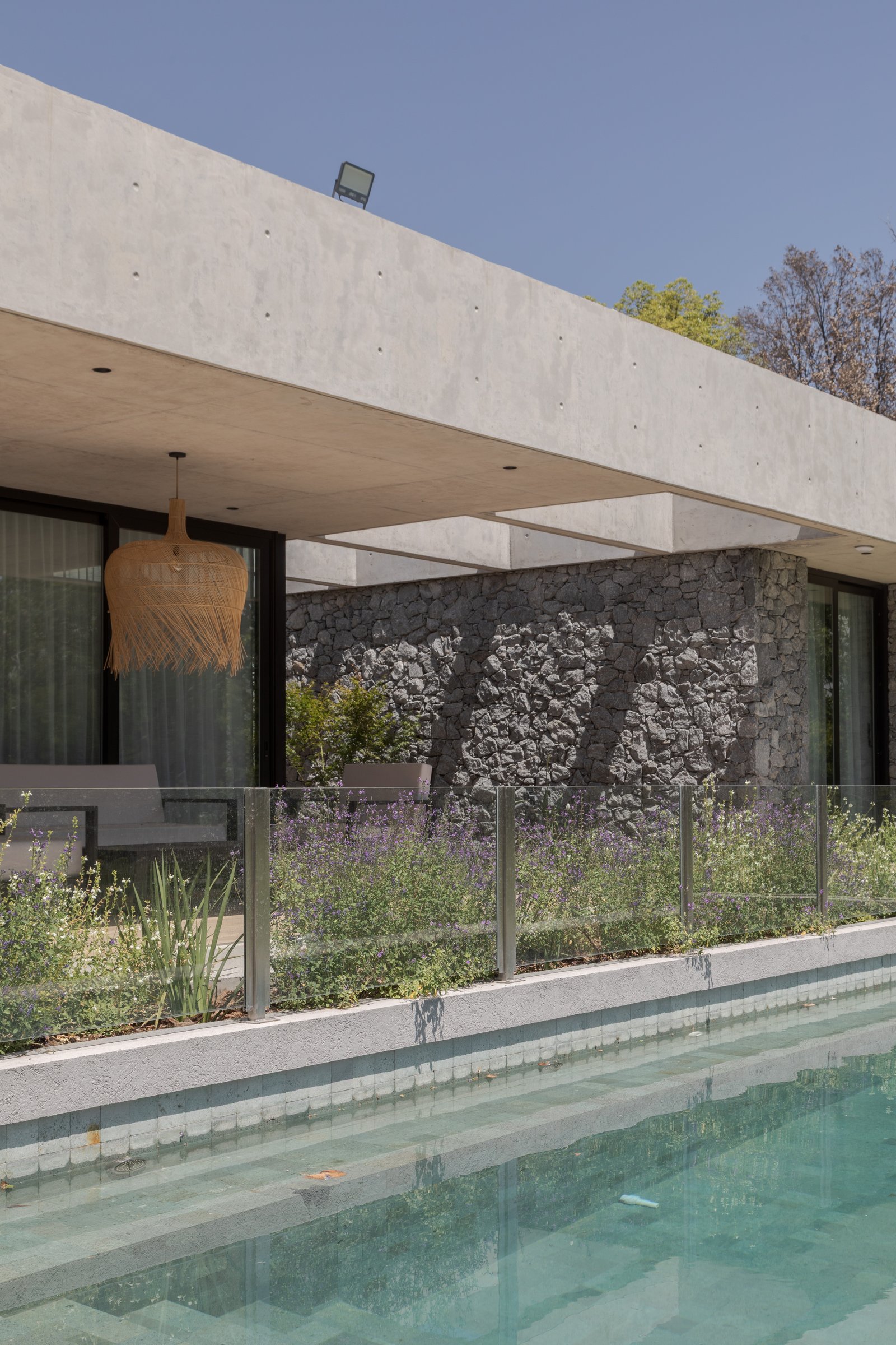 Pileta moderna con techo de hormigón, muros de piedra y vegetación exuberante — proyecto Casa PLANALTO, por Grupo CRBN, en Av. Pres. Perón 10298