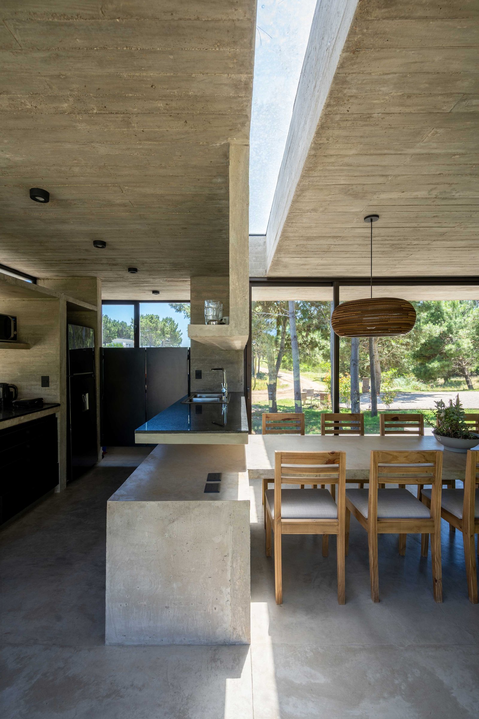 Cocina moderna de hormigón visto con isla y mesa de comedor — proyecto Casa Senderos, por Besonías Almeida arquitectos, en X6VF+67
