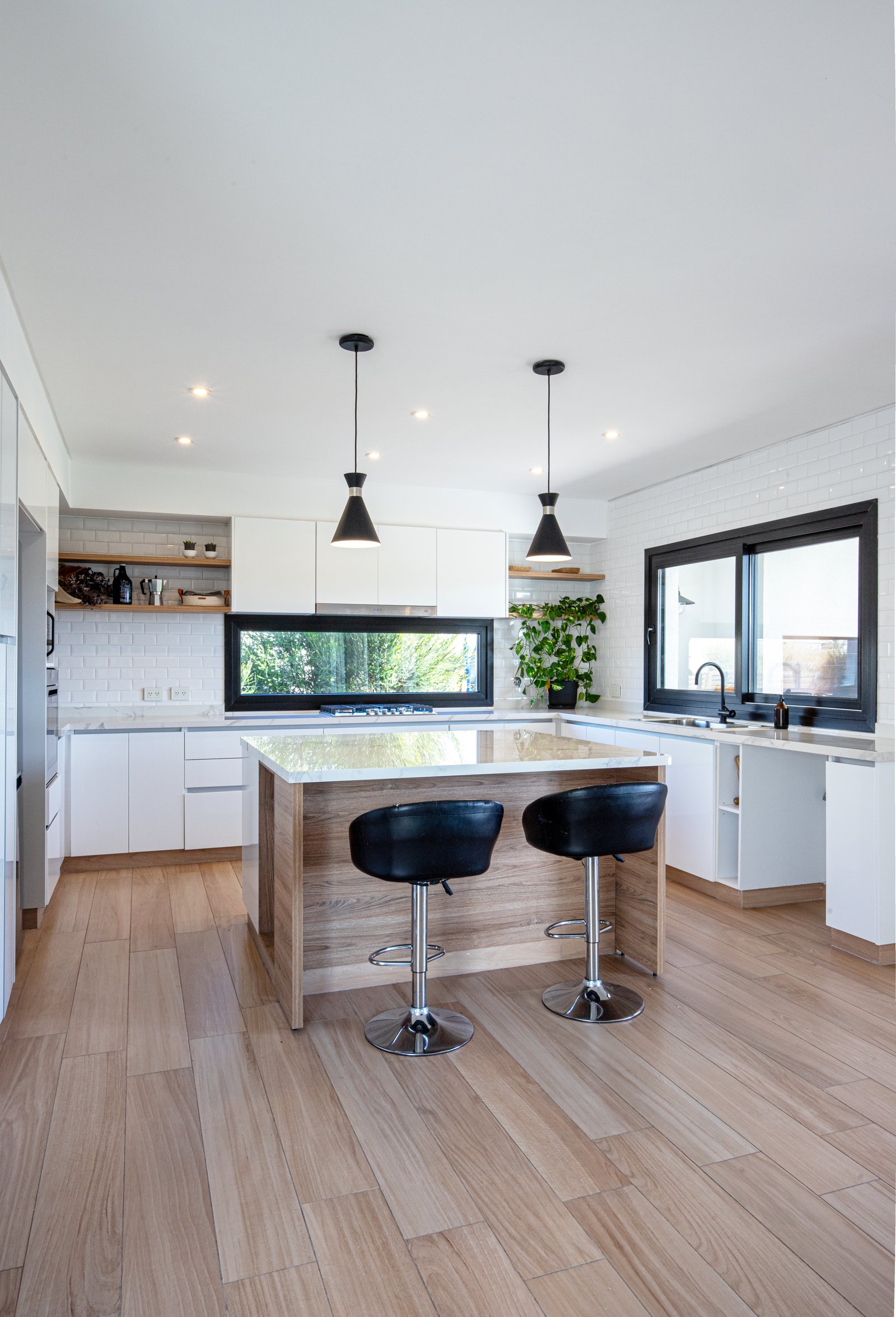 Cozinha moderna com ilha, janela panorâmica e luminárias pendentes — projeto SS45, por EZ architects, em Pilar