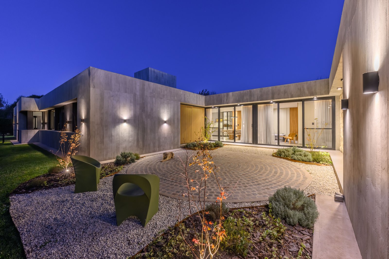 Fachada moderna brutalista de noche con asientos verdes y patio circular — proyecto La Paloma :: Villa Allende - Córdoba :: Paisajismo Residencial :: STIPA Arte Nat, por STIPA Arte